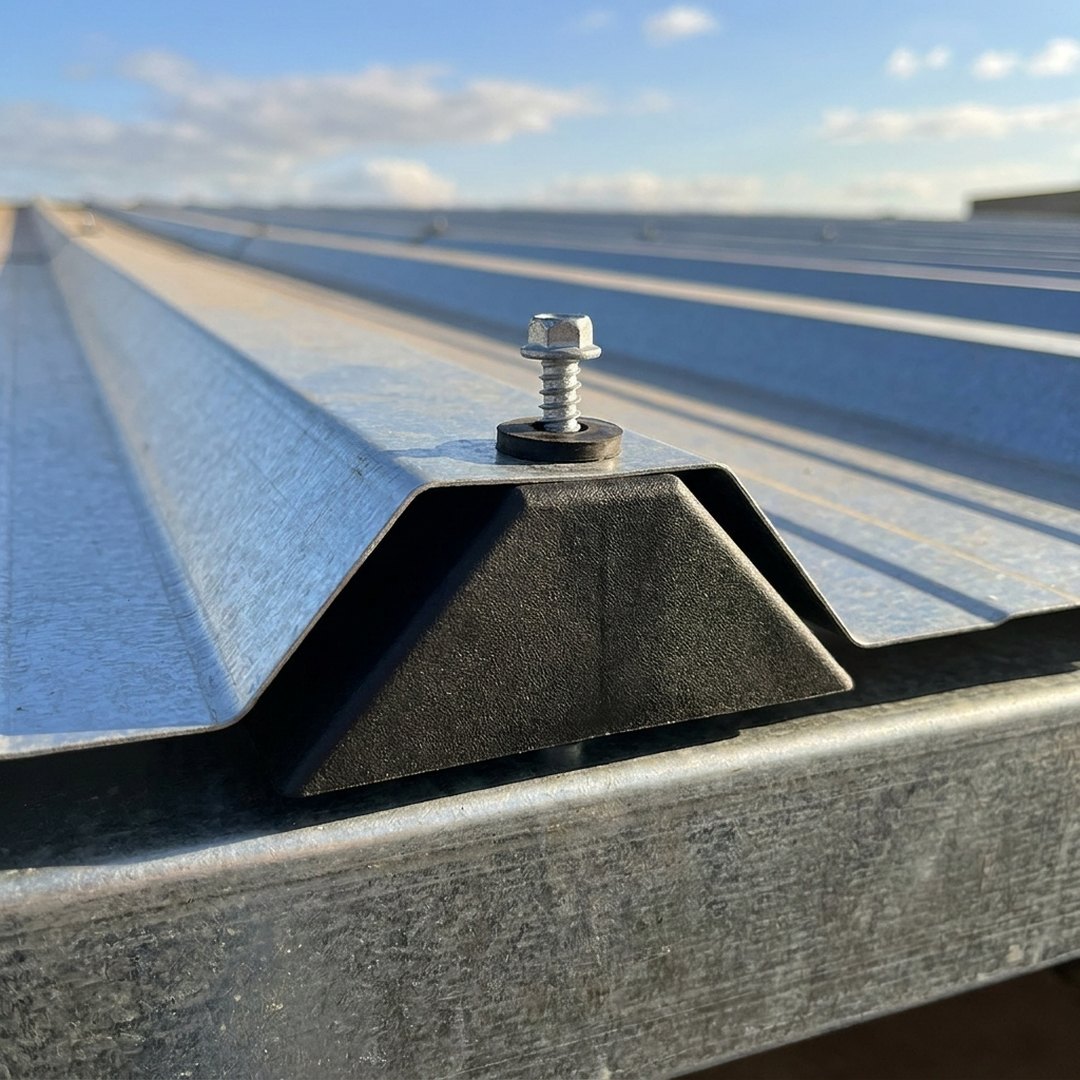 Calço T40 preto instalado sob a crista de uma telha metálica trapezoidal, com parafuso de fixação